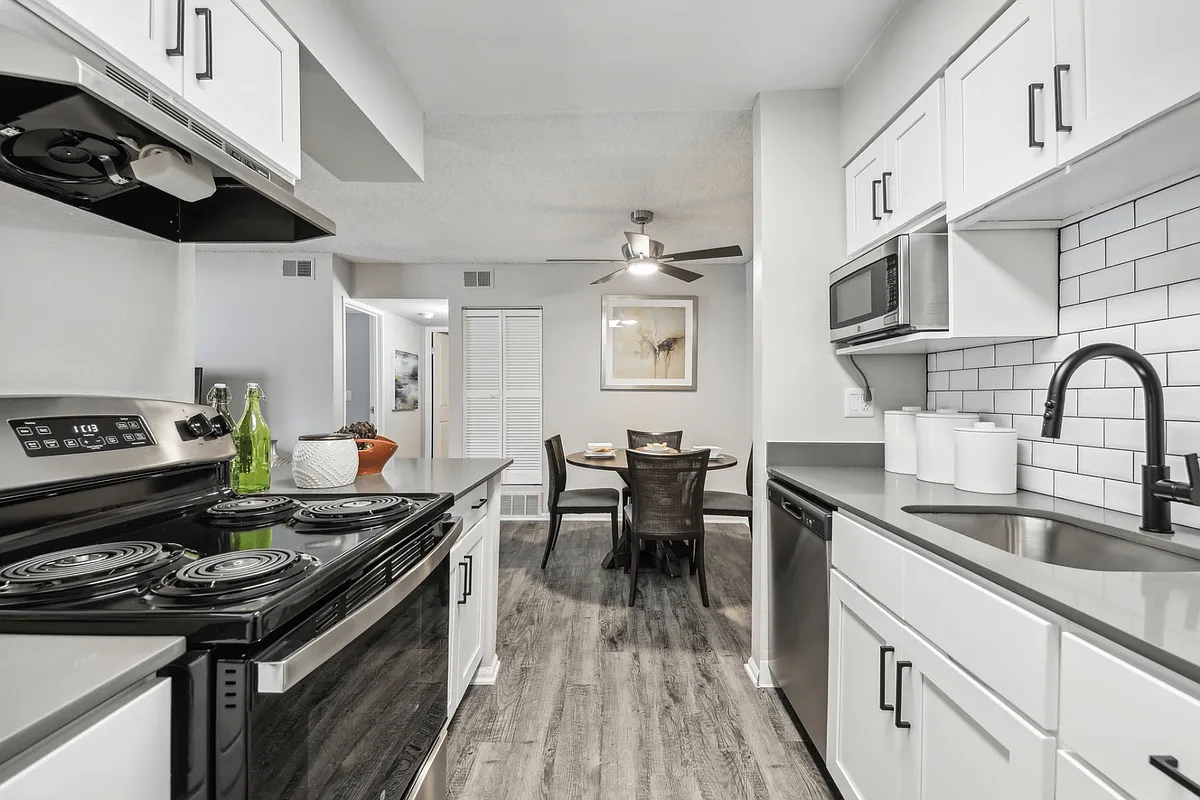 Modern kitchen with white cabinets, black appliances, and a dining area - Avery Park