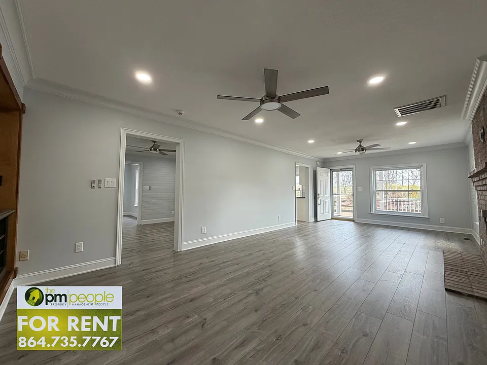 The living room is spacious, with built in shelf storage, exposed brick adding a rustic vibe, and LED can lights providing ample lighting.