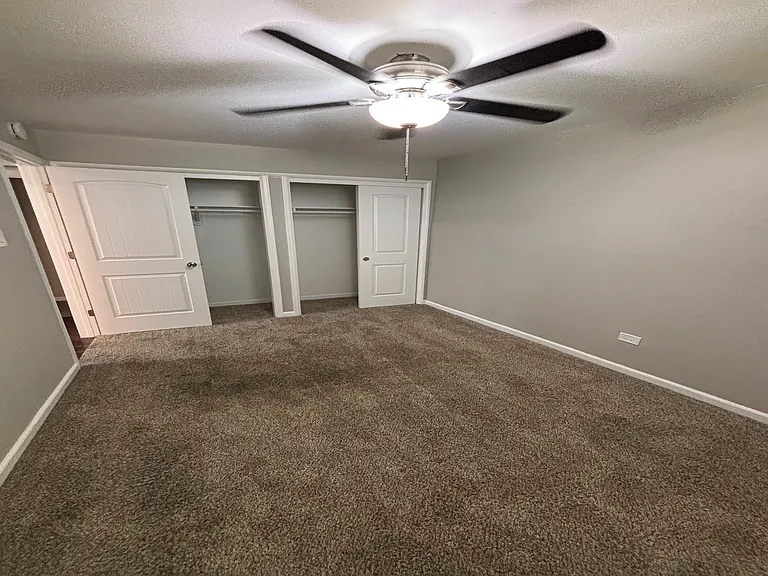 Bright bedroom featuring soft carpet, a ceiling fan, and double closet doors, offering comfort and ample storage.