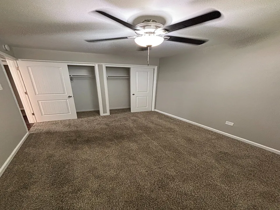 Bright bedroom featuring soft carpet, a ceiling fan, and double closet doors, offering comfort and ample storage.