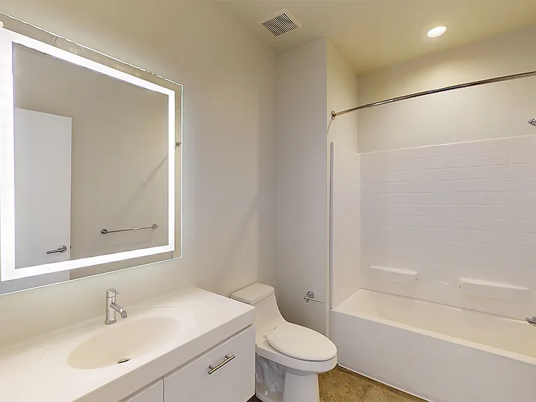 Apartment bathroom with wood-style flooring and an LED vanity mirror.