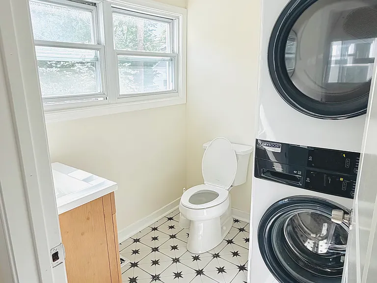 First-floor bathroom showing vanity, toilet, and stacked Electrolux washer/dryer _ all on stylish black and white star-pattern tile.