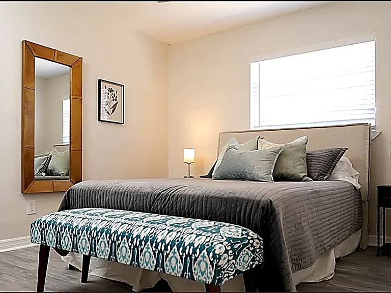 Stylishly furnished private bedroom with queen bed, full-length mirror, nightstands, and warm lighting