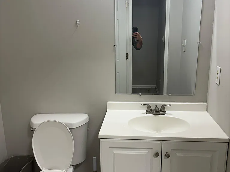Bathroom vanity area with sink, mirror, and under-cabinet storage beside the toilet for daily convenience.