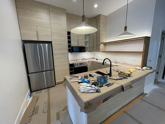 In progress phot of kitchen. Has an island with room for stools. Under cabinet lighting, new appliances.