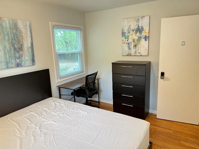 Furnished bedroom with a full-size bed, work desk and chair, dresser storage, and a window with blinds for natural light.