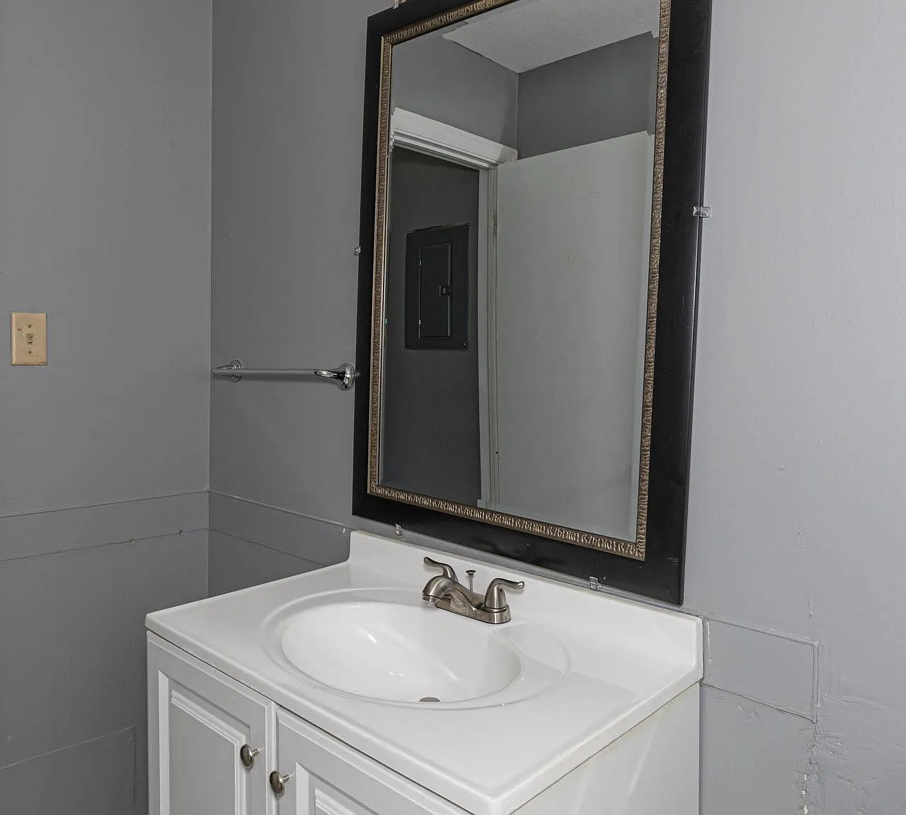 Bathroom vanity area with a white sink cabinet, framed mirror, and overhead lighting for daily routines.