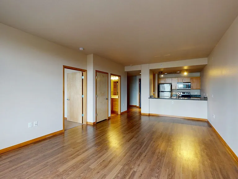 Apartment kitchen with stainless steel appliances, dining and living room with wood-style flooring.