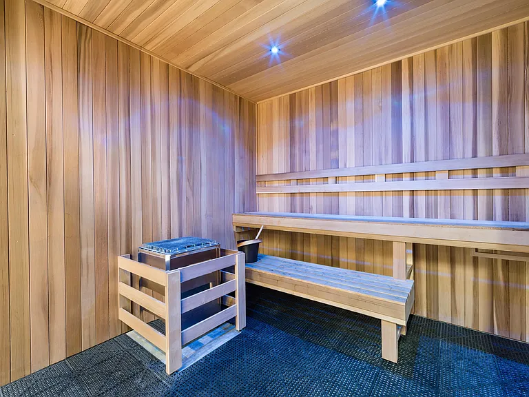 Wood-lined sauna with tiered bench seating and ambient lighting, offering a warm retreat for recovery and post-workout relaxation.