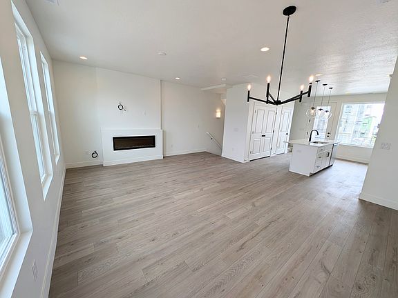 Open-concept living space with light wood floors, white walls, a modern fireplace, large windows, a