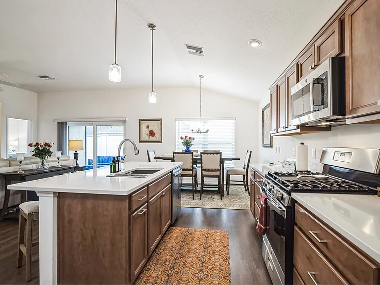 A View through the Kitchen to the Dining Room Area, Showcasing Cabinets, the Island, Sink, Stove, Microwave, Dishwasher, and Open Counter Space.