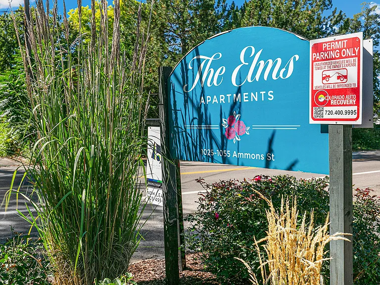 Charming entrance sign of The Elms Apartments framed by lush greenery, showcasing a welcoming community atmosphere.
