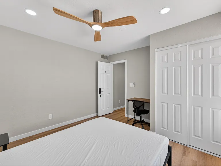 Private bedroom with wood-style flooring, a ceiling fan, and a sliding-door closet, plus space for a compact desk setup.