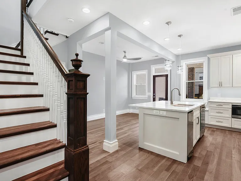 island dishwasher and trash compactor in island with center sink and high faucet; dining area in front of island; open walkway to basement with electric panel beside door.