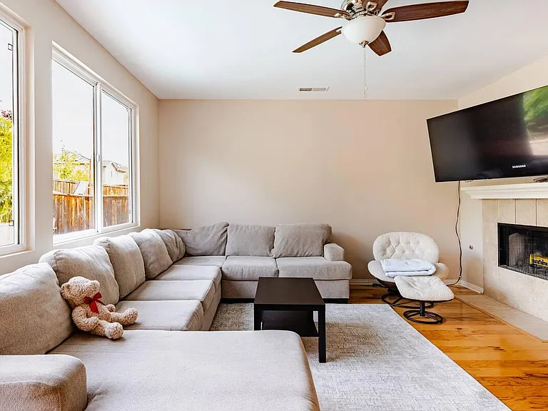Spacious living room with large windows, sectional seating, ceiling fan, and a fireplace with mounted TV for easy lounging.