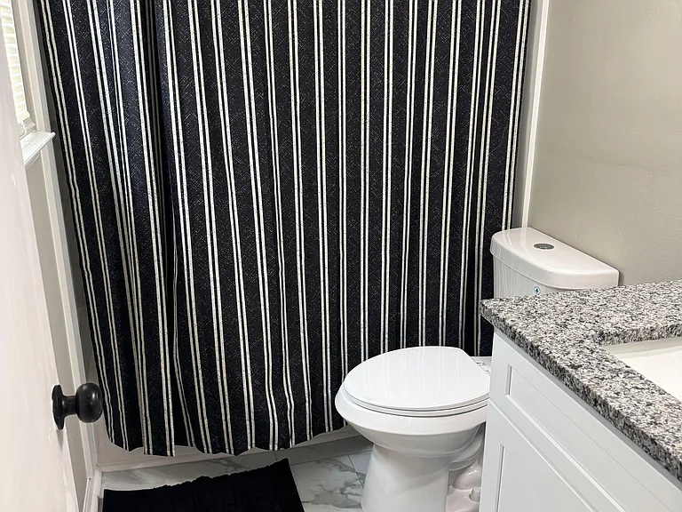 Functional bathroom with a tub/shower combo, vanity with stone-look countertop, and easy-clean tile flooring.