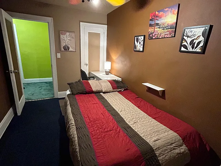 Furnished bedroom with a comfortable bed, ceiling fan, and a work desk setup, plus easy access to the hall.