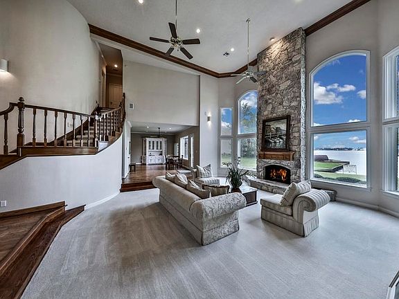 Two story stone fireplace accompanied by a wall of windows showcasing the lake.