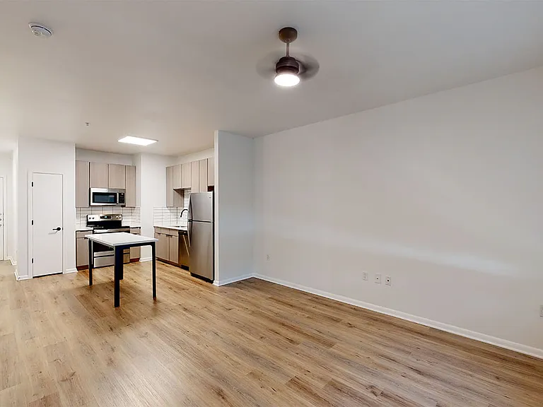 Apartment kitchen with stainless steel appliances, dining and living room with wood-style flooring.