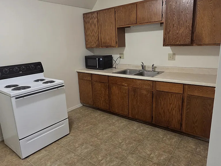 Functional kitchen with electric range, microwave, double basin sink, generous cabinet storage, and easy-clean tile flooring.