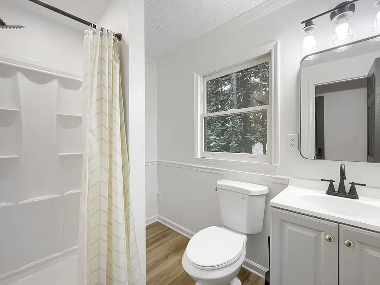 Full bath features a shower, single-sink vanity with storage, and a window for ventilation and natural light.