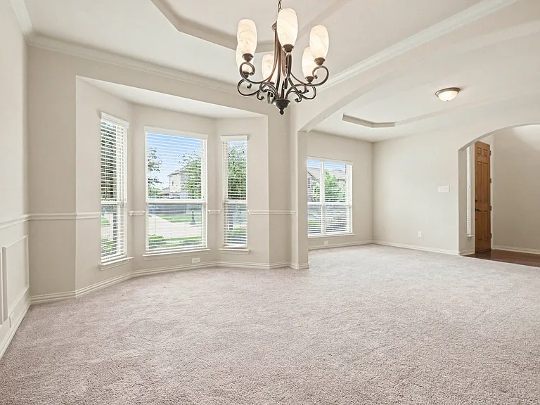 Spacious room featuring a bay window, tray ceiling, chandelier, recessed lighting, and wall paneling