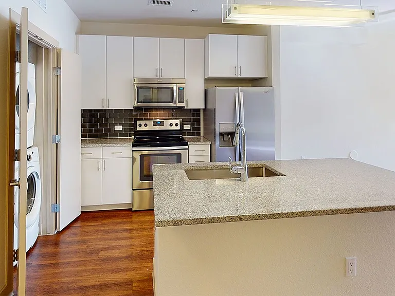 Apartment kitchen with stainless steel appliances, granite countertops and wood-style flooring.