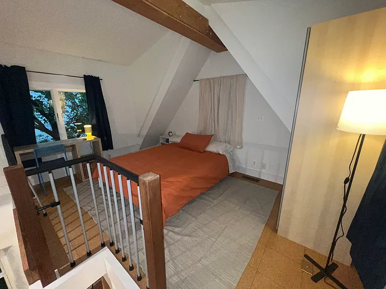 Loft bedroom with queen bed, full-length mirrored wardrobe and dedicated workspace at the far window with new desk, chair and task lighting.