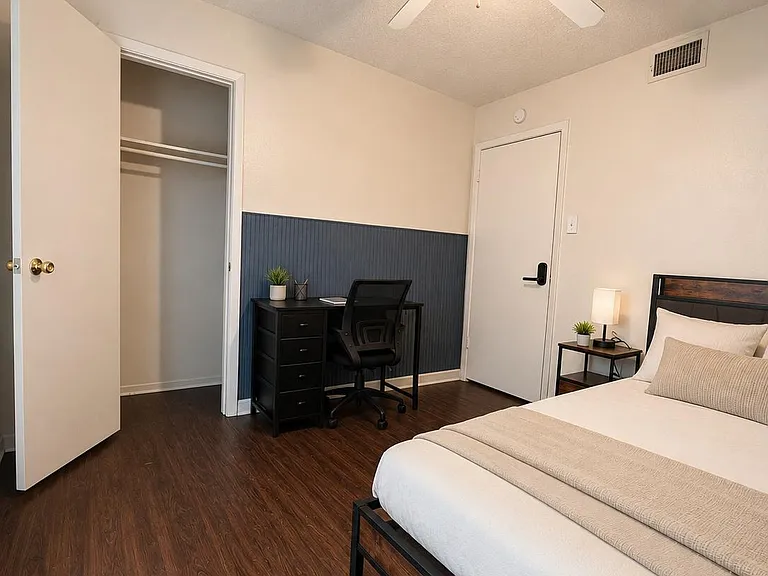 Furnished bedroom with wood-look floors, ceiling fan, open closet, and a dedicated desk workspace with nightstand lighting.