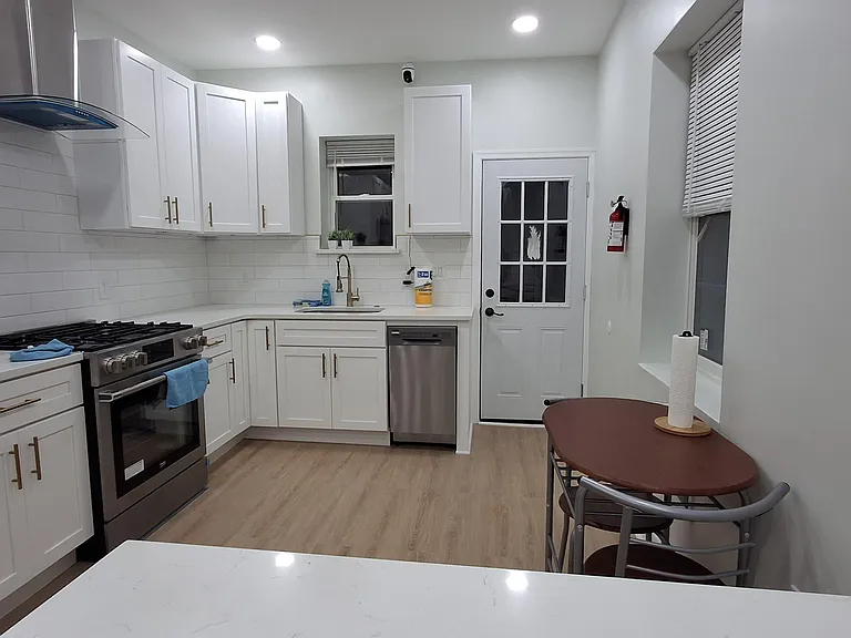 Updated kitchen with ample white cabinetry, subway-tile backsplash, gas range, dishwasher, and a small eat-in table.