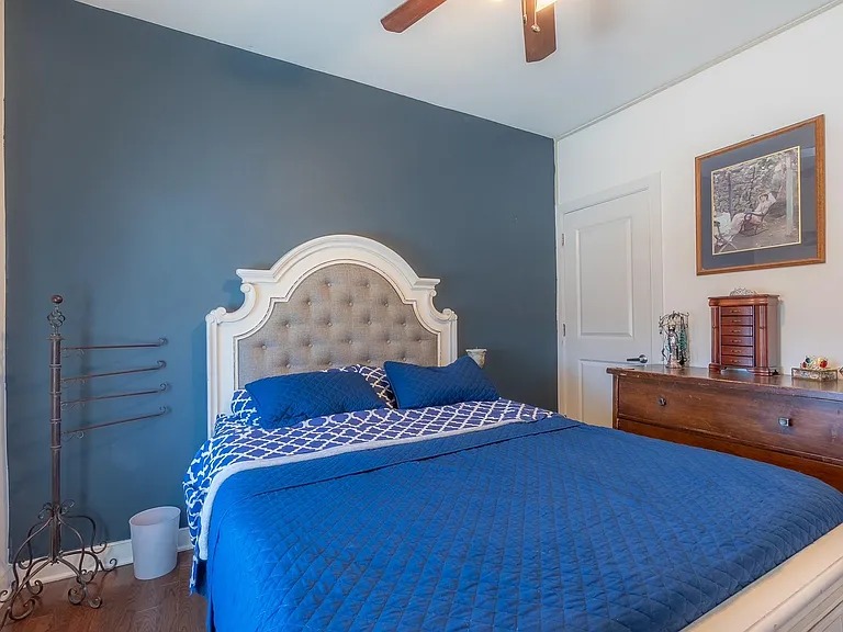 Furnished bedroom with a queen bed, accent wall dresser storage, and ceiling fan for added comfort.