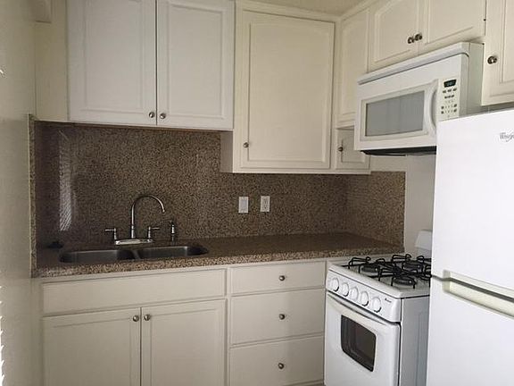 Kitchen sink with granite countertop, white cabinets, and appliances