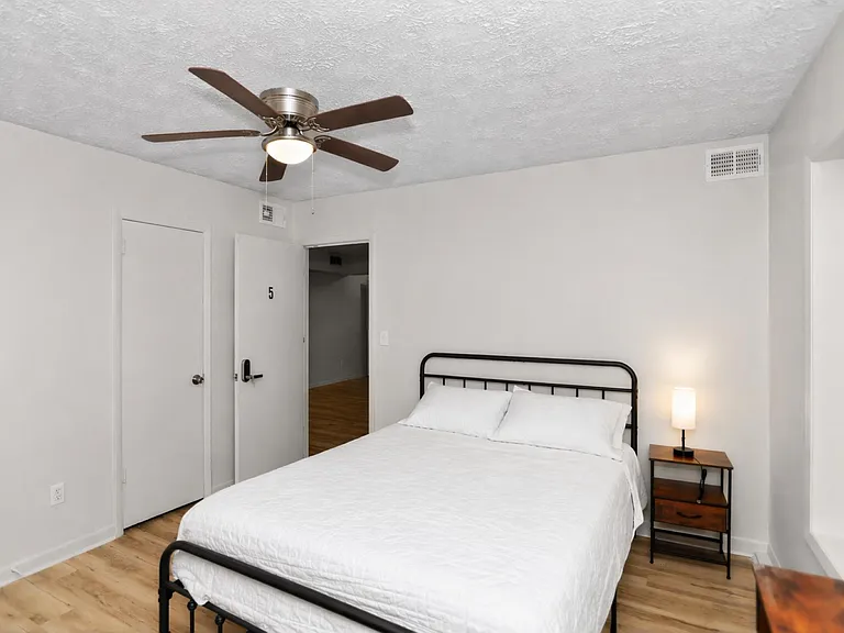 Furnished bedroom with a full bed, nightstand, ceiling fan with light, and wood-look flooring for comfortable everyday living