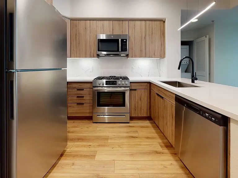 Apartment kitchen with stainless steel appliances, light counters, and wood style floor.