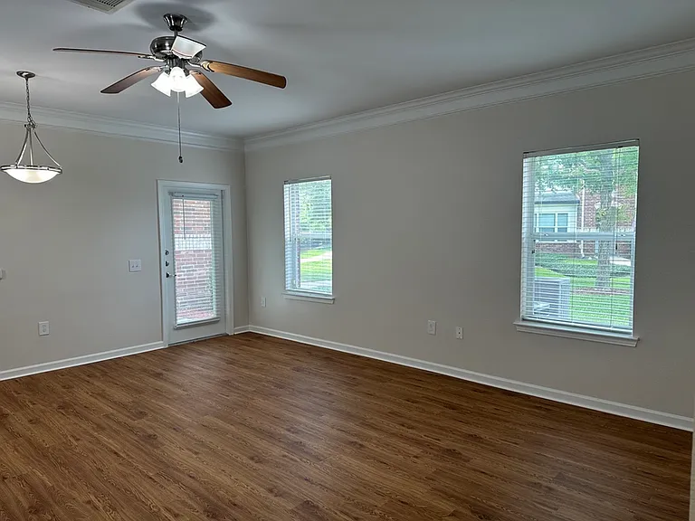Bright and spacious living room with elegant ceiling fan, wood-style flooring, and large windows offering natural light. Bright and spacious living room with elegant ceiling fan, wood-style flooring, and large windows offering natural light.