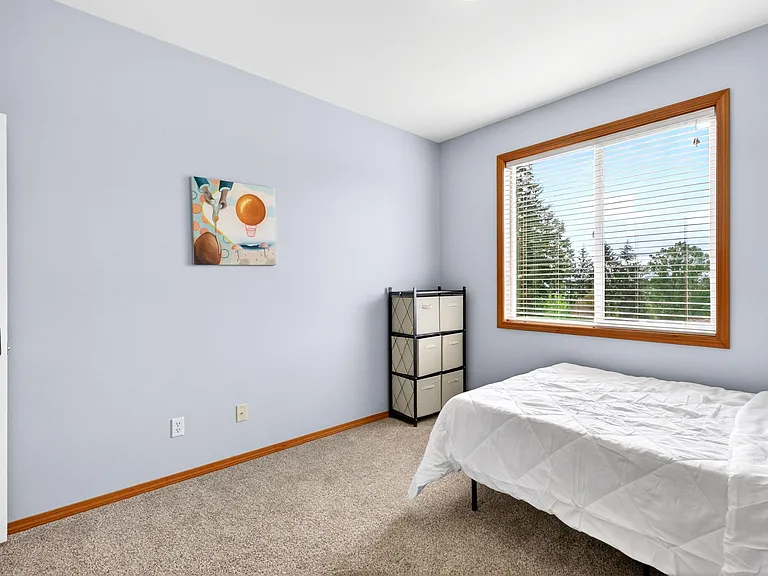 Private bedroom with carpeted floors, a large window with blinds, and space for a full bed plus storage.