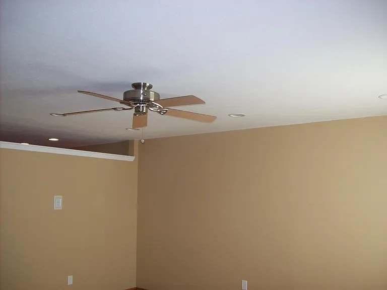 ceiling fan in living room and opening above wall dividing k