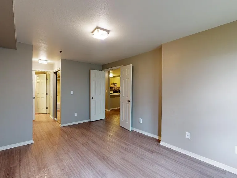 Spacious apartment bedroom with attached bathroom and wood-style flooring.