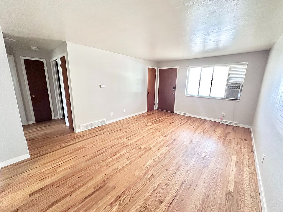 Bright living room with polished hardwood floors, a large window, and modern wall-mounted air conditioning, offering a spacious and airy ambiance.