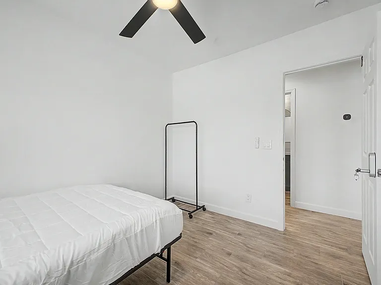 Minimalist bedroom with wood-look floors, ceiling fan, and space for a bed plus storage or a desk.