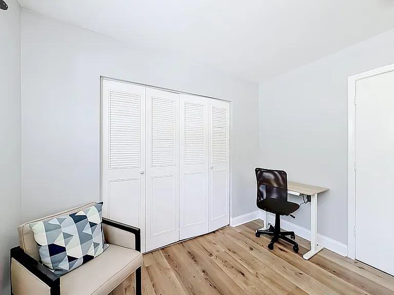 Versatile room with wide double-door closet, wood-style flooring, and a dedicated desk nook for working or studying.