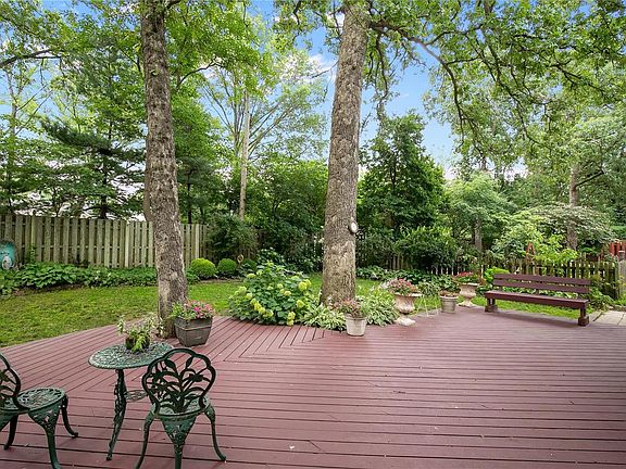 A beautiful & serene backyard setting with a freshly painted deck, an abundance of shade, and lush seasonal landscaping.