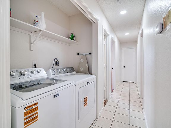 Dedicated laundry nook with full-size washer and dryer, plus wall shelving for supplies and easy access off the hallway.