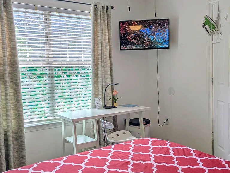 Bedroom with a large window, desk workspace, and mounted TV, offering a comfortable layout for relaxing and studying.