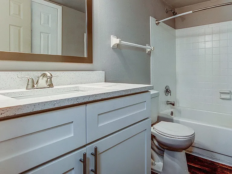 Contemporary bathroom with a sleek white vanity, elegant mirror, and tile bathtub, offering a clean and modern aesthetic.