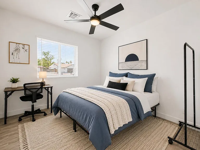 Well-sized bedroom with a ceiling fan, large window with blinds, and space for a desk plus clothing rack.
