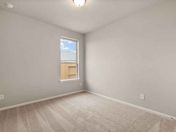 The secondary bedroom features plush carpet, neutral paint and a large window.