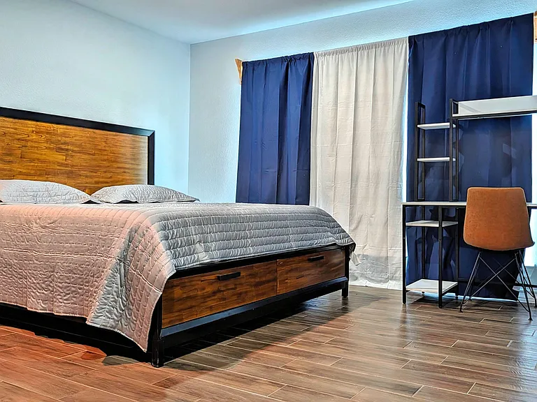 Furnished bedroom with a platform bed, under-bed storage, and a dedicated desk setup near the window.