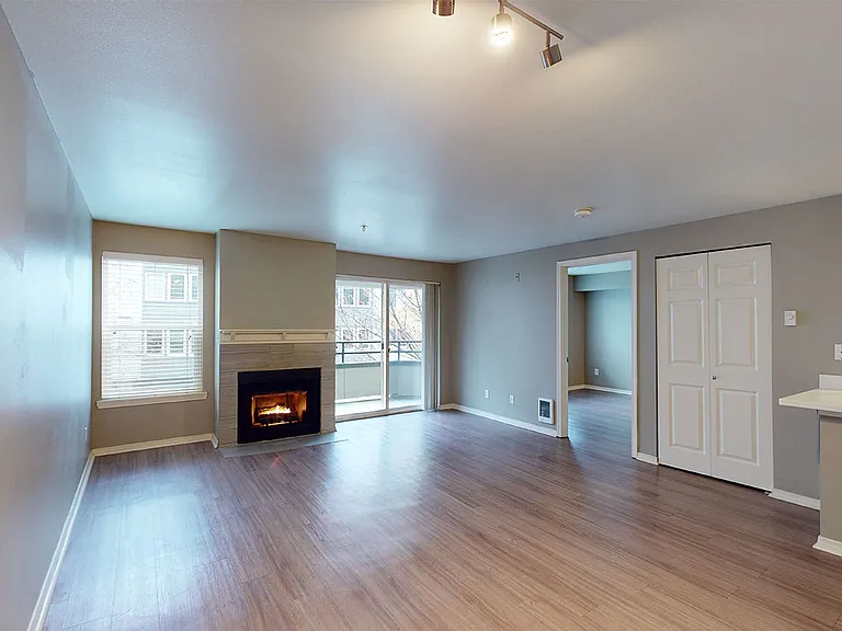 Apartment living room with wood-style flooring, fireplace, and balcony in select homes.