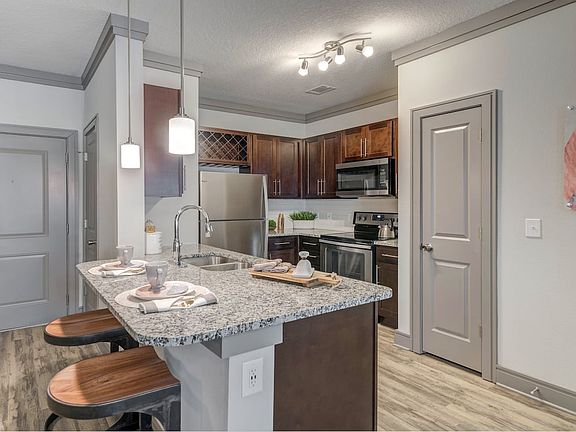 Modern kitchen with wood cabinetry, white tile backsplash, granite countertops, stainless steel appliances, and hard-surface flooring